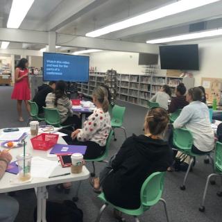 A dozen teachers in a room, facing a screen, watching a presentation. 